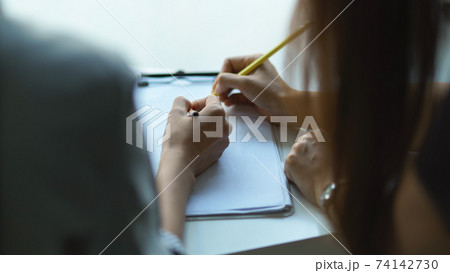 Two people hand writing on blank paper on clipboard while consulting on their work 74142730