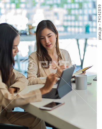 Two businesswomen working together with office supplies in meeting room Two businesswomen working together with office supplies in meeting room 74142839
