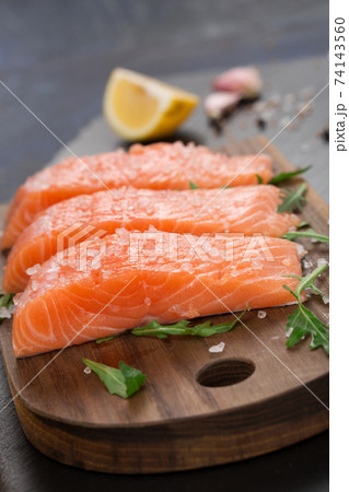 Raw fillet of salmon with sea salt, lemon and pepper on black stone background. Raw fillet of salmon with sea salt, lemon and pepper on black stone background. 74143560