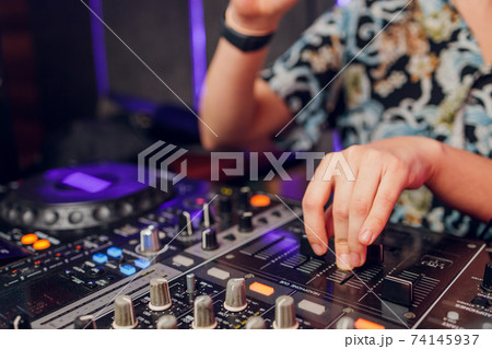 DJ's hand over the laptop and mixing console controlling the sound settings. DJ's hand over the laptop and mixing console controlling the sound settings. 74145937
