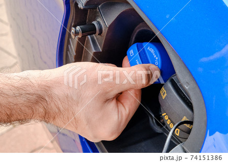 Close up mans hand opening a tank for Ad Blue fluid of a blue car. Diesel exhaust fluid or DEF for reduction of air pollution, October 2020, Prague, Czech Republic Close up mans hand opening a tank for Ad Blue fluid of a blue car. Diesel exhaust fluid or DEF for reduction of air pollution, October 2020, Prague, Czech Republic 74151386