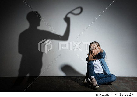 Domestic violence, abusing. Scared little caucasian girl, victim sitting close to white wall with shadow of angry father's threatening on it. Domestic violence, abusing. Scared little caucasian girl, victim sitting close to white wall with shadow of angry father's threatening on it. 74151527