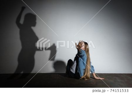Domestic violence, abusing. Scared little caucasian girl, victim sitting close to white wall with shadow of angry threatening mother with alcohol addiction. 74151533