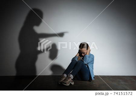 Domestic violence, abusing. Scared little caucasian girl, victim sitting close to white wall with shadow of angry threatening mother with alcohol addiction. 74151572