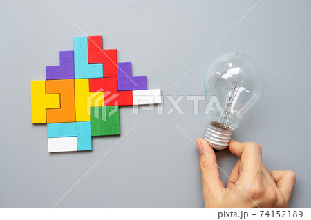 Hand holding lightbulb with colorful wood puzzle piece on gray background. New Idea, Creative, Innovation, Imagination, inspiration, Solution, Strategy and Logic concept Hand holding lightbulb with colorful wood puzzle piece on gray background. New Idea, Creative, Innovation, Imagination, inspiration, Solution, Strategy and Logic concept 74152189