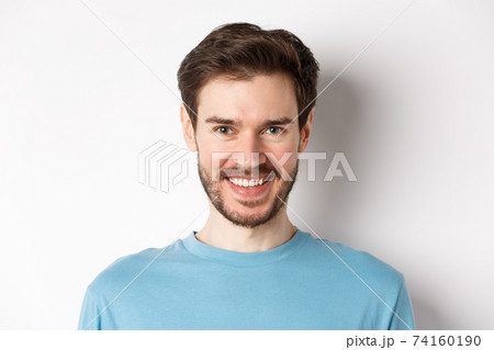 Close-up of handsome caucasian man smiling with white teeth, looking confident at camera, standing in blue shirt on white background Close-up of handsome caucasian man smiling with white teeth, looking confident at camera, standing in blue shirt on white background 74160190