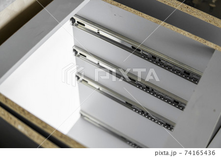 Stainless telescopic bayonet drawer slide guides, installed on a kitchen cabinet from gray chipboard. Accessories for carpentry used in the construction of furniture. Custom kitchen installation. 74165436