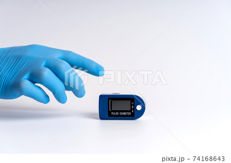 Pulse oximeter on a white background. A hand in a medical glove holds a device for health diagnostics 74168643