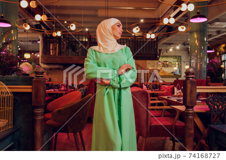 beautiful Muslim girl in hijab smiling, waiting for her food in a restaurant. 74168727
