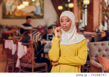 beautiful Muslim girl in hijab smiling, waiting for her food in a restaurant. 74168747