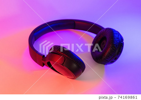 Stylish black wireless headphones lit with colorful neon light on abstract background isolated. Modern technology concept with copy space Stylish black wireless headphones lit with colorful neon light on abstract background isolated. Modern technology concept with copy space 74169861