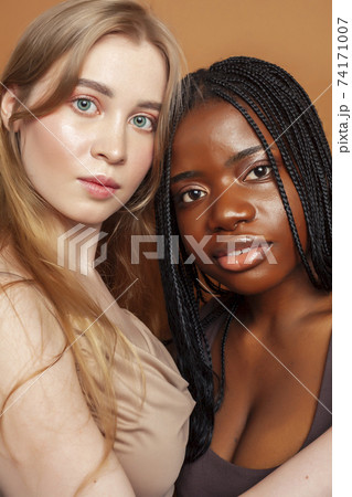 two pretty girls african and caucasian blond posing cheerful together on brown background, ethnicity diverse lifestyle people concept two pretty girls african and caucasian blond posing cheerful together on brown background, ethnicity diverse lifestyle people concept 74171007
