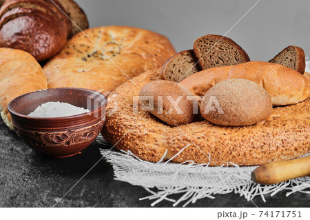 Various types of bread on dark table with bowl of flour 74171751