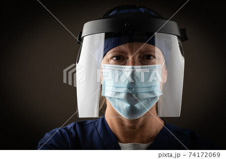 Female Medical Worker Wearing Protective Face Mask and Gear Against Dark Background Female Medical Worker Wearing Protective Face Mask and Gear Against Dark Background 74172069