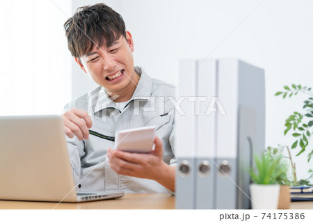 会社で電卓を見てショックを受ける作業服を着た男性 74175386