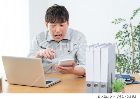 会社で電卓を見てショックを受ける作業服を着た男性 74175392