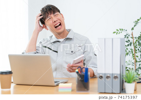 会社で電卓を見てショックを受ける作業服を着た男性 74175397