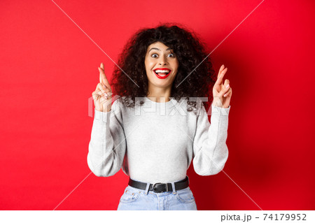 Hopeful excited woman making a wish, cross fingers for good luck and smiling amazed at camera, praying for dream come true, waiting for results, red background Hopeful excited woman making a wish, cross fingers for good luck and smiling amazed at camera, praying for dream come true, waiting for results, red background 74179952