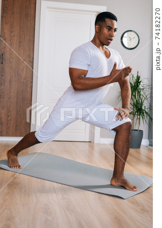 Focused fit African-American man making sport fitness exercise standing on yoga mat. Focused fit African-American man making sport fitness exercise standing on yoga mat. 74182270