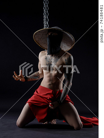 Slender samurai in a red raincoat and an Asian hat with a chain - Slavery and freedom 74186481