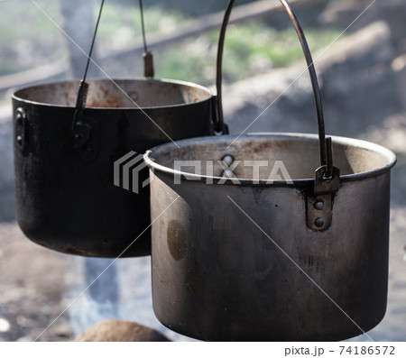 Cooking in two sooty old cauldrons on campfire at sunny day Cooking in two sooty old cauldrons on campfire at sunny day 74186572