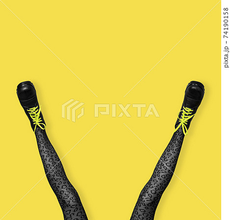 New gray female boots with bright yellow laces on long slender woman legs in gray tiger print tights isolated on yellow background. New gray female boots with bright yellow laces on long slender woman legs in gray tiger print tights isolated on yellow background. 74190158