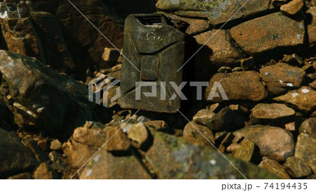 Old rusty metal canister for gasoline fuel at rocks 74194435