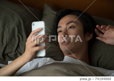 ベッドでスマートフォンを見る男性 74194660