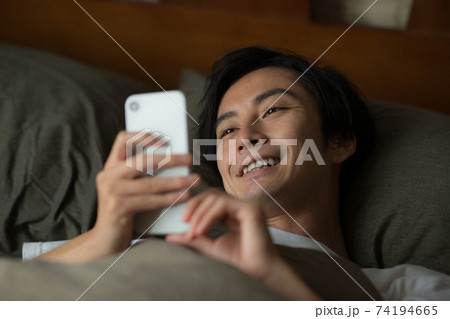 ベッドでスマートフォンを見る男性 ベッドでスマートフォンを見る男性 74194665