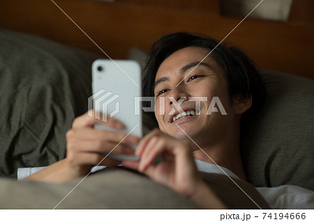 ベッドでスマートフォンを見る男性 ベッドでスマートフォンを見る男性 74194666