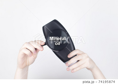 Chemical components on the shampoo label: Mineral oil. Female hands hold a magnifying glass on the jar, which indicates the harmful ingredient. White background, place for your text 74195874