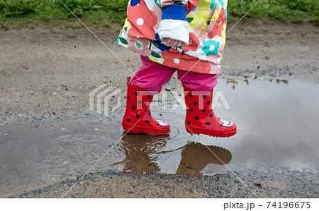 A little girl in a bright jacket and red boots jumps merrily through puddles. 74196675