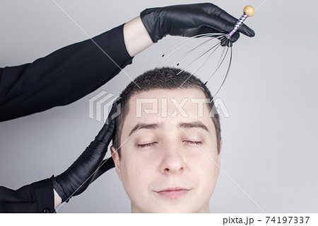A man is given a head massage with a capillary massager in the salon. The client's face shows relaxation and joy. The concept of anti-stress massage and the provision of services by a masseur. A man is given a head massage with a capillary massager in the salon. The client's face shows relaxation and joy. The concept of anti-stress massage and the provision of services by a masseur. 74197337