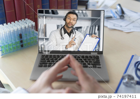 Doctor in front of a laptop monitor during an online video call. Conversation with a colleague. 74197411