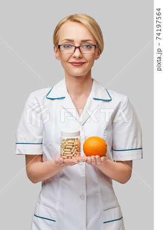 nutritionist doctor healthy lifestyle concept - holding fresh organic orange fruit and vitamin capsules nutritionist doctor healthy lifestyle concept - holding fresh organic orange fruit and vitamin capsules 74197564