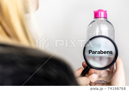 A woman examines the harmful ingredients of the micellar waterthrough a magnifying glass. Means with parabens. The concept of hazardous substances in cosmetics and household chemicals A woman examines the harmful ingredients of the micellar waterthrough a magnifying glass. Means with parabens. The concept of hazardous substances in cosmetics and household chemicals 74198768