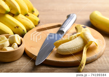 Ripe banana fruit with kitchen knife on wooden cutting board Ripe banana fruit with kitchen knife on wooden cutting board 74199384