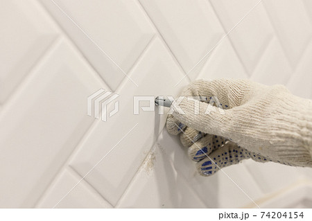 Worker's hand in glove inserts wall pvc dowel in wall cladded with tile ceramic Worker's hand in glove inserts wall pvc dowel in wall cladded with tile ceramic 74204154