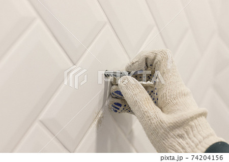 Worker's hand in glove inserts wall pvc dowel in wall cladded with tile ceramic Worker's hand in glove inserts wall pvc dowel in wall cladded with tile ceramic 74204156
