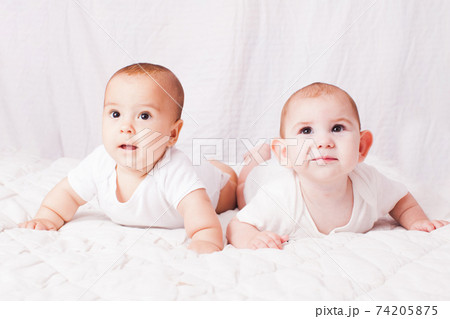 Two baby twins lying on the stomach at the white Two baby twins lying on the stomach at the white 74205875
