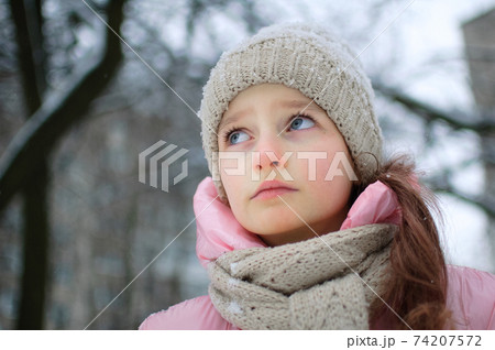 Sad child girl in warm knitted winter clothes spent time outdoors and got frozen. 74207572