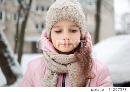 Sad child girl in warm knitted winter clothes spent time outdoors and got frozen. 74207573