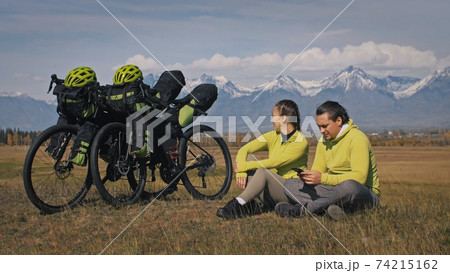 The man and woman travel on mixed terrain cycle touring with bikepacking. The two people journey with bicycle bags. Mountain snow capped. 74215162