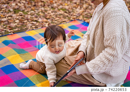 秋の公園でママとタブレットpcで遊ぶ赤ちゃんの写真素材