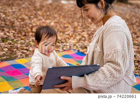 秋の公園でママとタブレットpcで遊ぶ赤ちゃんの写真素材