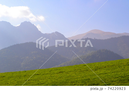 Green meadow in front of mountains in a slight haze. Spring nature and freshness. Green meadow in front of mountains in a slight haze. Spring nature and freshness. 74220923