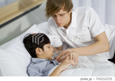 Young father takes care of his sick  adopted son in bed. The boy tried to take medicine to improve the health condition. 74222255