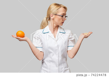 nutritionist doctor healthy lifestyle concept - holding fresh organic orange fruit and vitamin capsules 74224478