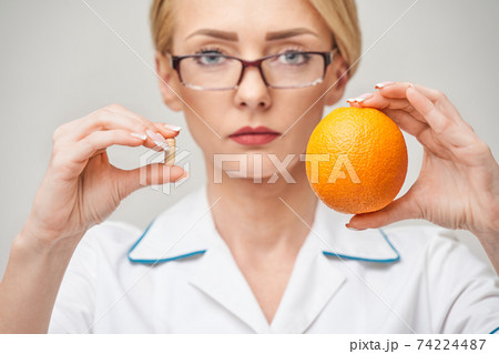 nutritionist doctor healthy lifestyle concept - holding fresh organic orange fruit and vitamin capsules 74224487