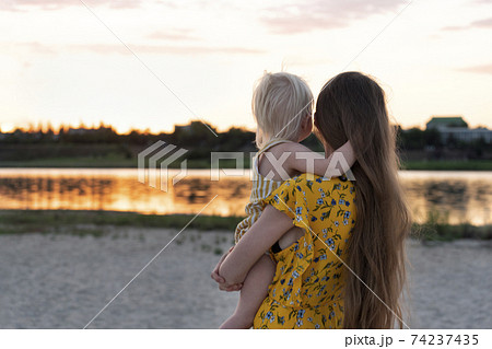 Young mother holding baby and watching the sunset over the water. 74237435